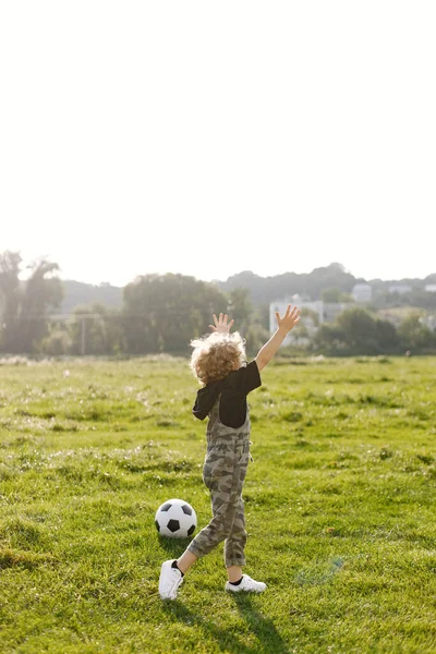 小屁孩在公园里玩球 男孩总体上穿着卡其布 小男孩拿着球站在草地上 — 图库照片