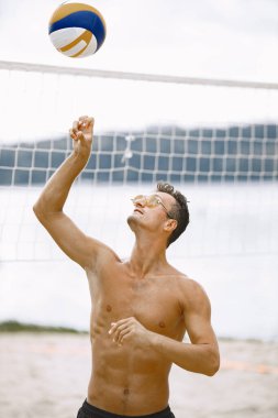 Voleybol oynayan atletik adam. Güneş gözlüğü takıyor, kumsalda..