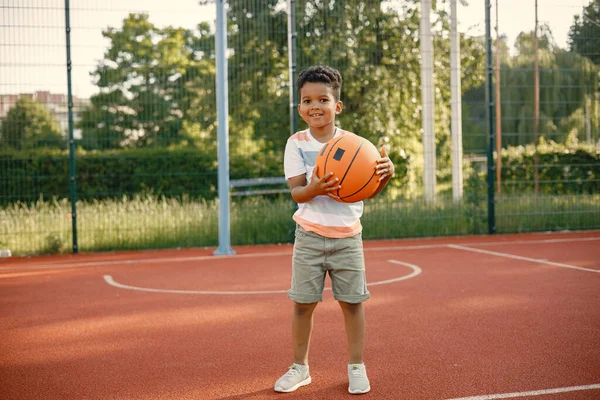 小男孩站在公园附近的篮球场上 穿着白色T恤的男孩 男孩打篮球 — 图库照片