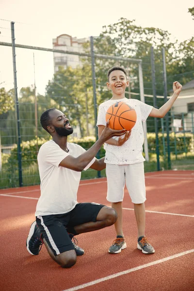 年轻的父亲和他的儿子站在公园附近的篮球场上 男人和男孩穿着白色的T恤 男孩摆姿势拍照 假装自己是赢家 — 图库照片