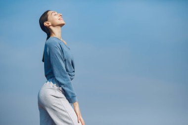 Gökyüzü arka planında eğitim alan güzel bir kız. Mavi kazaklı kadın. Bayan yoga yapıyor.