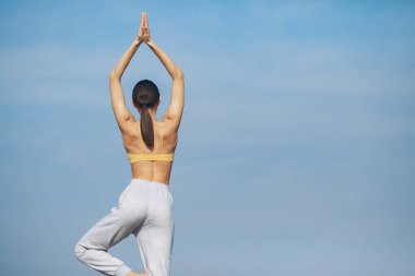 Gökyüzü arka planında eğitim alan güzel bir kız. Sarı bluzlu kadın. Bayan yoga yapıyor.