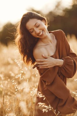 Woman in a summer field. Brunette in a brown sweater. Girl on a sunset background.