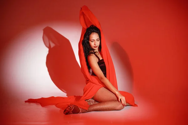 stock image Curly brunette girl posing for a photo. Girl wearing velour bodysuit and is wrapped in red scarf. Projectors light girl up.