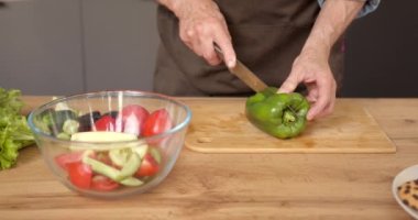Olgun, mutlu bir adam evde sağlıklı yiyecekler hazırlıyor, modern mutfak içinde taze sebze salatası kesiyor..