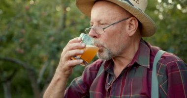 Gülümseyen erkek çiftçi, güz hasadı sırasında meyve bahçesindeki cam şişede elma suyu gösteriyor. Hasat zamanı..