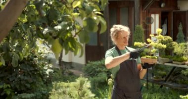 Genç adam bahçede rahatla. Bitkileri, çiçekleri ve ölü yaprakları kesmeyi önemsiyor. Doğa, hobi konsepti.