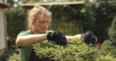 Genç adam bahçede rahatla. Bitkileri, çiçekleri ve ölü yaprakları kesmeyi önemsiyor. Doğa, hobi konsepti.