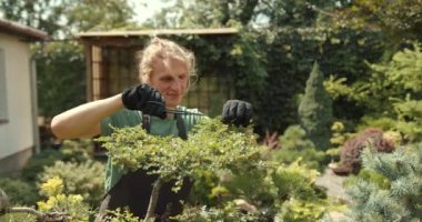 Genç adam bahçede rahatla. Bitkileri, çiçekleri ve ölü yaprakları kesmeyi önemsiyor. Doğa, hobi konsepti.