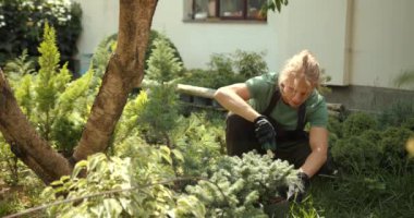 Genç adam bahçede rahatla. Bitkileri, çiçekleri ve ölü yaprakları kesmeyi önemsiyor. Doğa, hobi konsepti.