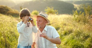 Küçük çocuk sahada dürbünle yukarı bakıyor. Dünyayı keşfetmek. Yaz tatili. Açık hava aktiviteleri.