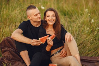 Couple in a field. Woman in a black blouse. Sunset background. People with watermelon.