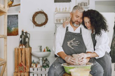 Ortak yaratıcı çalışma. Günlük giysiler ve önlükler içinde yetişkin, zarif bir çift. İnsanlar kilden bir stüdyoda çömlek çarkında kase yapıyorlar..