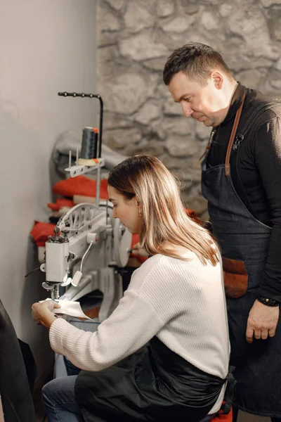 Mature craftsman with young woman working in workspace. Man and woman wearing an apron and repairing a shoe. Grounge dark stone texture background.