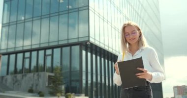 Resmi giysili beyaz bir iş kadını ofis binasının arka planında evrak tutuyor. İş merkezine yakın bir ofis çalışanı..