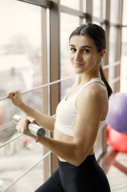 Jimnastik salonundaki büyük pencereli kız. Siyah tayt ve spor bluz giyen bir kız. Elinde dambıl tutan genç bir kadın..