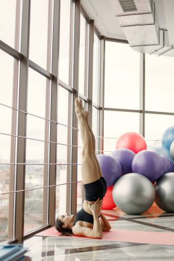 Jimnastik salonundaki büyük pencereli kız. Siyah tayt ve spor bluz giyen bir kız. Yoga yapan genç kadın..