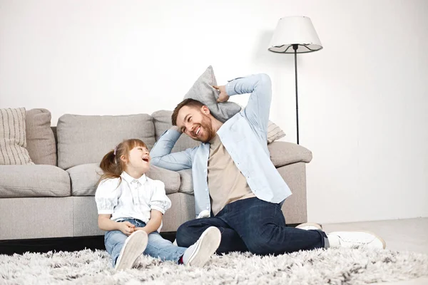 Loving father playing with his daughter with Down syndrome at home together. Man and girl sitting on a floor near sofa. Bearded man wearing blue shirt and girl white shirt.