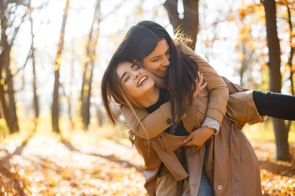 两个漂亮的女性朋友在一起 两个笑着的妹妹在秋天的公园里散步 拥抱着 穿着外套的布鲁内特和金发女孩 — 图库照片