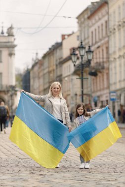 Genç anne ve kızı eski kasabanın caddesinde dikiliyorlar. Kız ve kadın ellerinde Ukrayna 'nın büyük bayrakları, mavi ve sarı renklerde. Kadın ve kız Ukrayna 'yı savaşa karşı destekliyor.