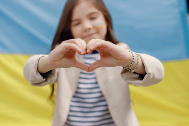 Ukrayna bayrağının önünde duran yanağında Ukrayna bayrağı olan küçük bir kız. Kalbini gösteren genç ve güzel bir kız. Ukrayna 'yı destekleyen kız.