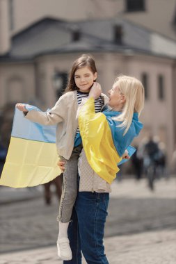 Genç anne ve kızı eski kasabanın caddesinde dikiliyorlar. Kız ve kadın ellerinde Ukrayna 'nın büyük bayrakları, mavi ve sarı renklerde. Kadın ve kız Ukrayna 'yı savaşa karşı destekliyor.