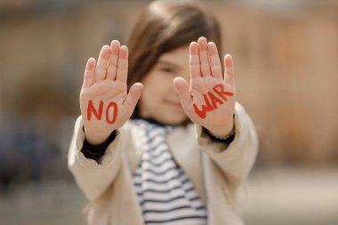 Küçük kız sokakta dururken avuçlarını gösteriyor. Genç ve güzel kız kelimeler yazdı. Avuçlarda savaş yok. Barış için ayakta duran kız.