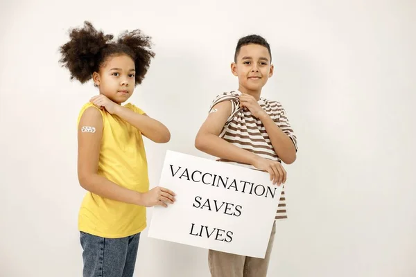 男孩和女孩孤零零地站在白色的背景上 接种疫苗后 儿童肩上有一条创可贴 海报上说疫苗可以拯救生命 — 图库照片