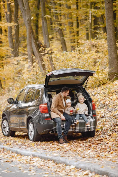 Happy family resting after day spending outdoor in autumn park. Father and two children sitting inside car trunk, smiling. Family holiday and traveling concept.