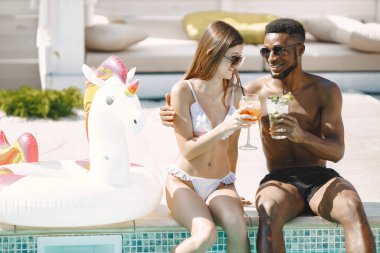 Beyaz kız ve siyah erkek arkadaşı yüzme havuzunun yanında dinleniyorlar. Beyaz mayo ve güneş gözlüğü takan bir kız. Zenci çocuk ve kız arkadaşı kokteyl içiyor..