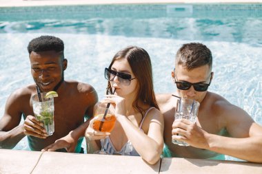 Genç kız ve iki tane çok ırklı erkek arkadaşı yüzme havuzunun yanında güneşleniyorlar. Beyaz mayo ve güneş gözlüğü takan bir kız. Siyah çocuk, beyaz erkek ve kız kokteyl içiyor..