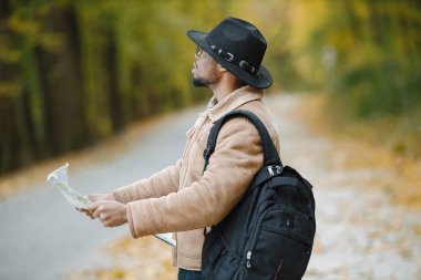Genç siyahi bir adam yolda otostop çekiyor ve elinde bir harita tutuyor. Erkek gezgin kendini kaybolmuş hissediyor, tek başına otostop ile seyahat ediyor. Kahverengi ceketli, siyah şapkalı ve sırt çantalı bir adam..