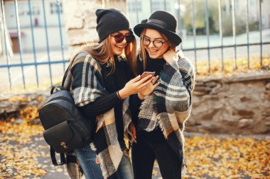 Güneşli yaz şehrinde yürüyen ve telefon kullanan iki şık genç kız.