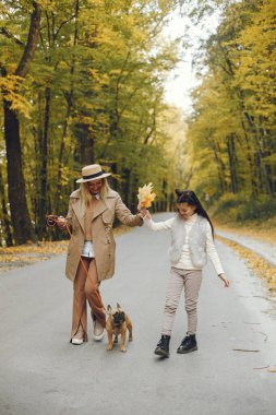 Kadın, küçük kız ve köpek sonbahar parkında yürüyor. Kahverengi buldog ve bayan sahipleri bir gün parkta oyun oynayıp eğleniyorlar. Bej ceketli ve şapkalı bir kadın..