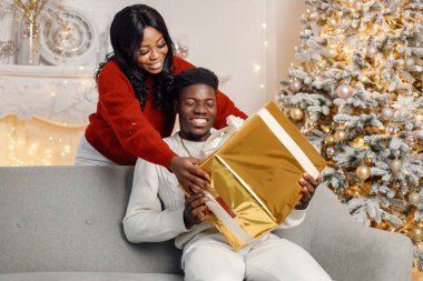 Noel arifesinde hediyeleri olan genç siyah bir çift. Evdeki arabada oturan bir adam. Esmer kadın arkada duruyor ve erkek arkadaşına bir hediye sunuyor..