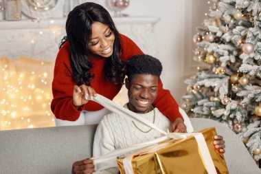 Noel arifesinde hediyeleri olan genç siyah bir çift. Evdeki arabada oturan bir adam. Esmer kadın arkada duruyor ve erkek arkadaşına bir hediye sunuyor..