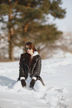 Close-up portrait of woman in black jacket. Woman standing in a forest in snowy day.