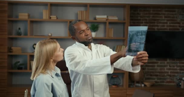 黑人男性和白人女性同事检查病人的报告 有经验的男牙医帮助他的女同事翻译办公室里病人的X光照片 — 图库视频影像