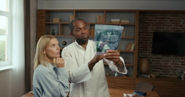黑人男性和白人女性同事检查病人的报告 有经验的男牙医帮助他的女同事翻译办公室里病人的X光照片 — 图库视频影像