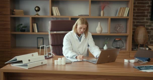 職場でラップトップを使用する女性医師 ポジティブな医師は質の高い医療を提供するために最善を尽くします — ストック動画