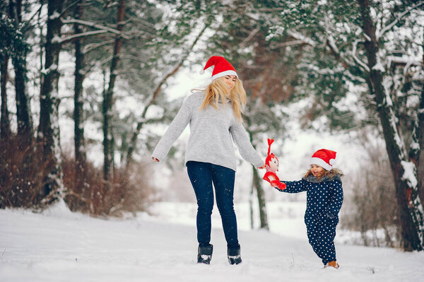 Family have fun in a winter park. Stylish mother in a gray sweater. Little girl in a red hat