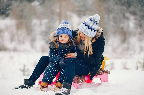 一家人在冬天的公园里玩得很开心 穿着黑色夹克的时髦妈妈 带着粉红雪橇的小女孩 图库图片