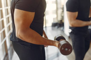 Spor salonundaki sporcular. Siyah bir adam egzersiz yapıyor. Siyah tişörtlü adam. Uluslararası arkadaşlar..