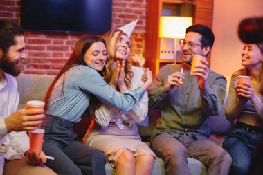 Genç arkadaşlar akşam partisinde arabada oturuyorlar. Ortadaki sarışın kızın doğum günü var ve parti konisi takıyor. Arkadaşlar ellerinde içeceklerle kağıt bardak tutuyorlar...