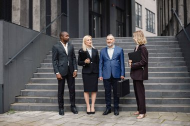 Modern ofis binasının önünde duran kendinden emin iş adamları. Erkekler ve kadınlar ellerinde belgelerle konuşuyor. Bankacılık ve finans piyasası kavramı.