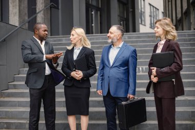 Modern ofis binasının önünde duran kendinden emin iş adamları. Erkekler ve kadınlar ellerinde belgelerle konuşuyor. Bankacılık ve finans piyasası kavramı.