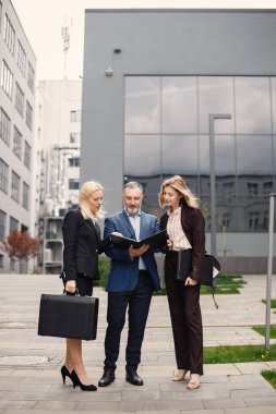 Modern ofis binasının önünde duran kendinden emin iş adamları. Kadın ve erkek konuşuyor ve ellerinde belgeler var. Bankacılık ve finans piyasası kavramı.