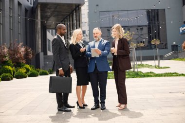 Modern ofis binasının önünde duran kendinden emin iş adamları. Erkekler ve kadınlar konuşuyorlar ve belgelere bakıyorlar. Bankacılık ve finans piyasası kavramı.