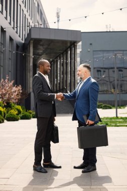 Modern ofis binasının önünde duran kendinden emin iş adamları. İki adam konuşuyor ve el sıkışıyor. Bankacılık ve finans piyasası kavramı.