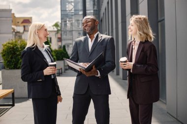 Modern ofis binasının önünde duran kendinden emin iş adamları. Siyahi adam ve beyaz kadın konuşuyorlar ve belgelere bakıyorlar. Bankacılık ve finans piyasası kavramı.